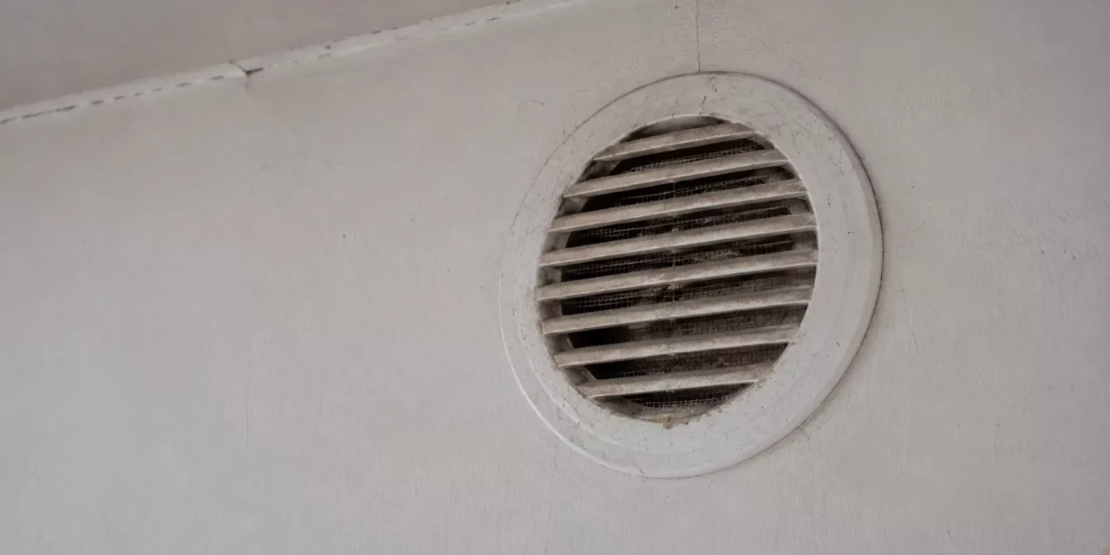 Grille d'aération ronde en plastique blanc empoussiérée sur un mur peint