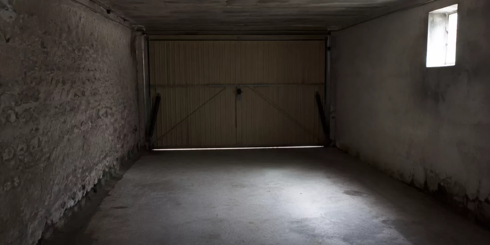 Intérieur de garage fermé, mur en pierre et bas de mur plus sombre le long du sol en béton