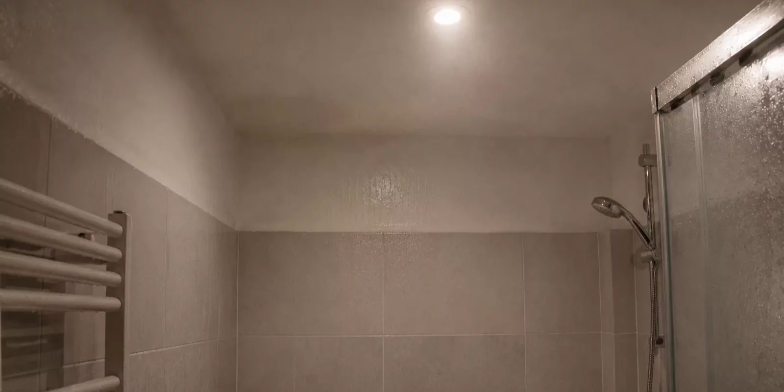 Salle de bain sans fenêtre remplie de vapeur après une douche, plafond éclairé par un spot