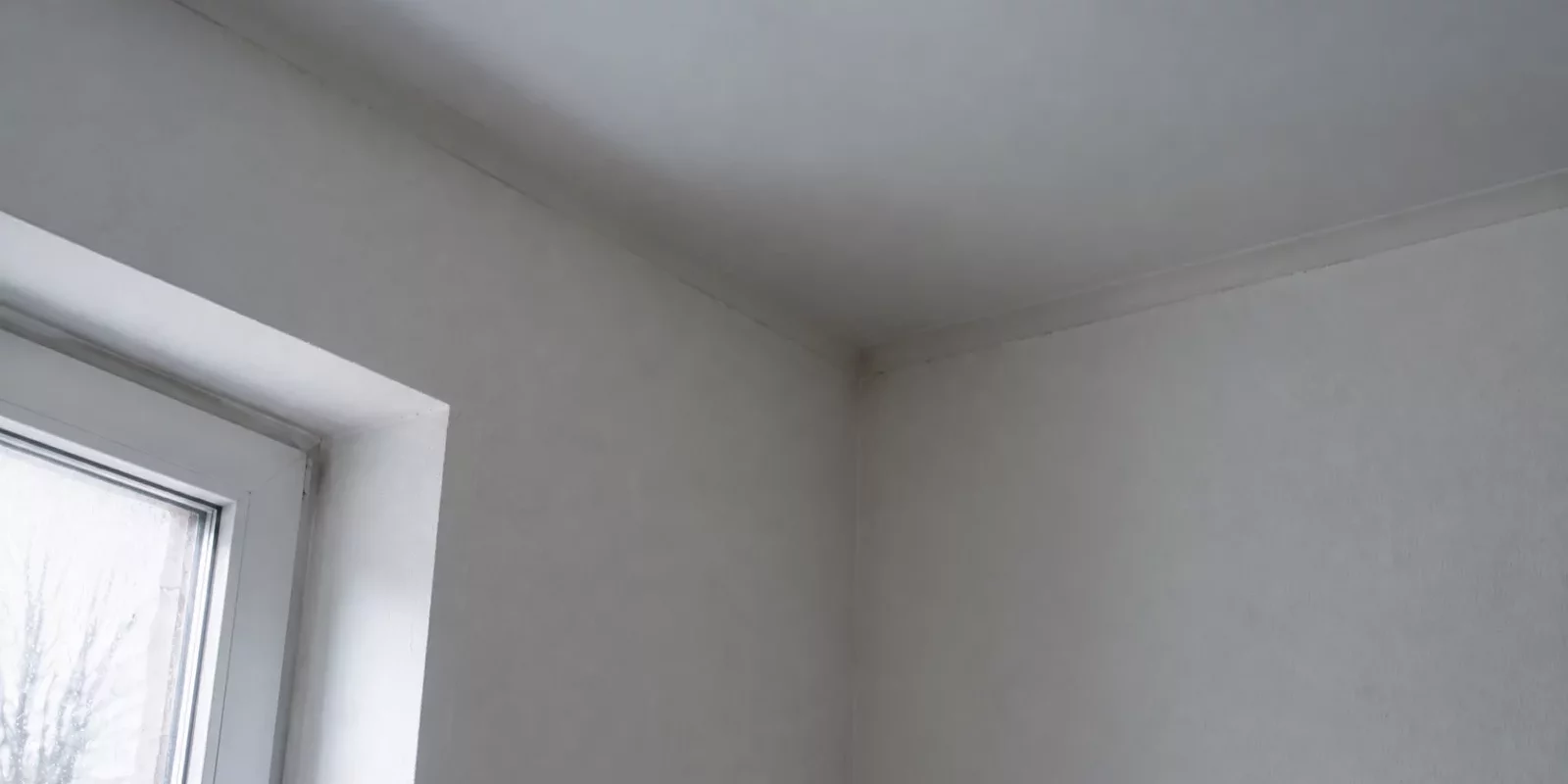 Jonction entre un mur et un plafond dans une pièce chauffée, près d'une fenêtre en hiver